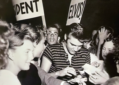 Elvis signing autographs in Hollywood amidst a sea of fans including signs that say "Elvis for President."