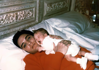 Elvis on his infamous 8x8 bed holding baby Lisa Marie on his chest